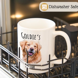 Op de afbeelding: Witte keramische mok met een lachende golden retriever en de tekst "Goldie's Mum". De mok is voorzien van het label "Dishwasher Safe".