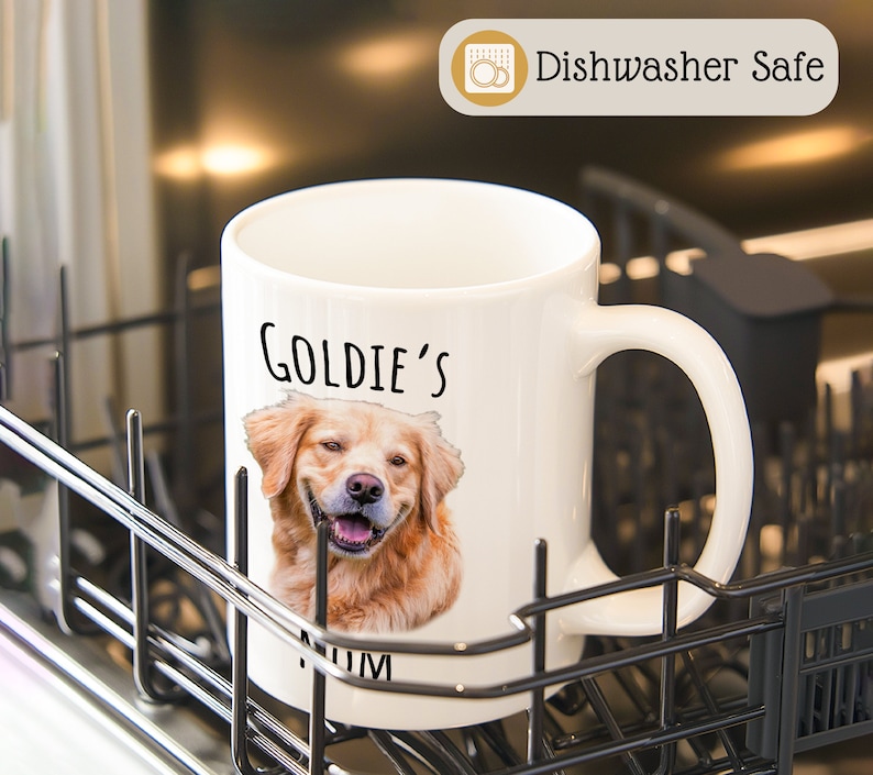 Op de afbeelding: Witte keramische mok met een lachende golden retriever en de tekst "Goldie's Mum". De mok is voorzien van het label "Dishwasher Safe".