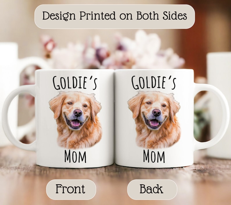 Op de afbeelding: Twee witte keramische mokken met een afbeelding van een golden retriever en de tekst "Goldie's Mom" erop. De mokken hebben een handvat aan de rechterkant. De tekst "Design Printed on Both Sides" staat bovenaan. De woorden "Front" en "Back" staan onderaan.