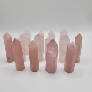 May include: A collection of twelve rose quartz crystal points, each with a natural, pointed tip and a smooth, polished surface. The crystals are arranged in a semi-circle on a white background.