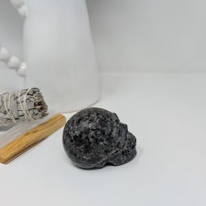 May include: A black and grey speckled stone skull sculpture.
