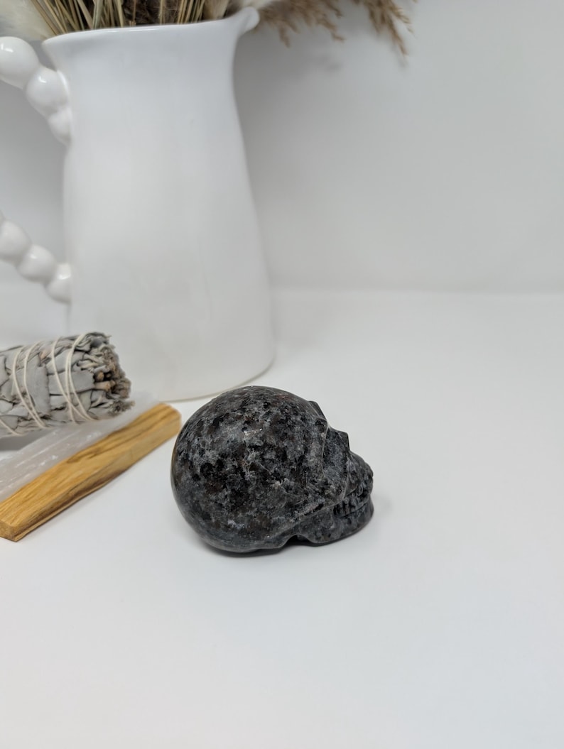 May include: A black and grey speckled stone skull sculpture.