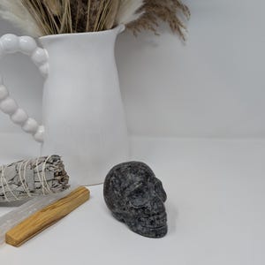May include: A black and grey skull made of polished stone. The skull is sitting on a white surface.