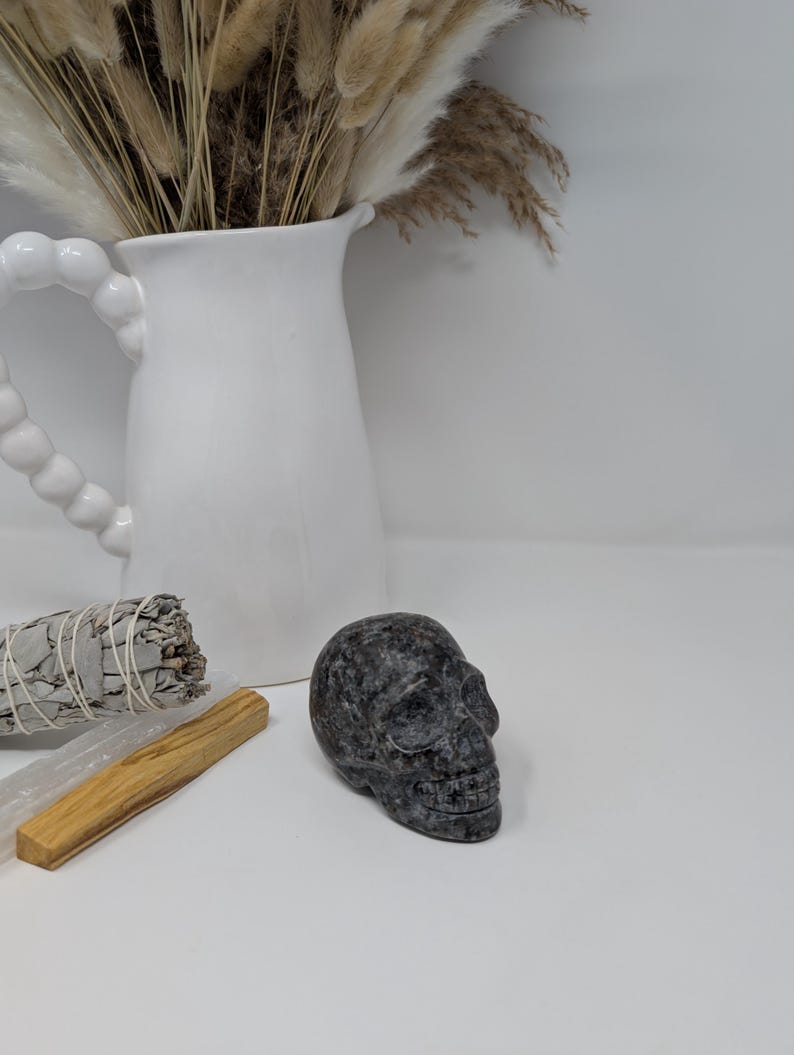 May include: A black and grey skull made of polished stone. The skull is sitting on a white surface.
