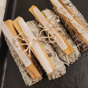 May include: Four bundles of white sage smudge sticks tied with white twine and gold thread. Each bundle includes a white selenite stick.