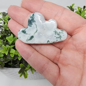 May include: A white and green agate stone carved into the shape of a cloud. The stone has a smooth, polished surface.