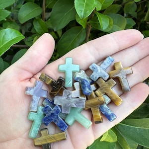 May include: A collection of small, colorful crystal crosses in various shades of green, blue, purple, and brown. The crosses are made of natural stones and are perfect for jewelry making or meditation.