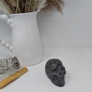 May include: A black and grey stone skull sculpture on a white surface.