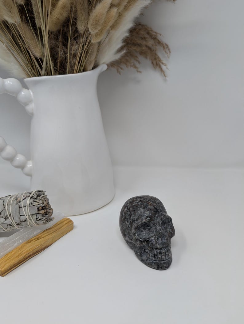 May include: A black and grey stone skull sculpture on a white surface.