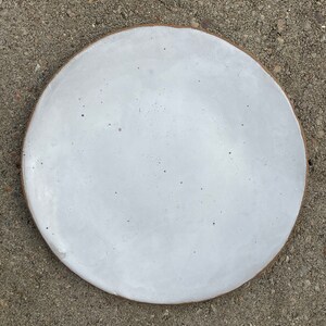 May include: A white ceramic plate with a slightly speckled finish. The plate has a subtle brown rim.