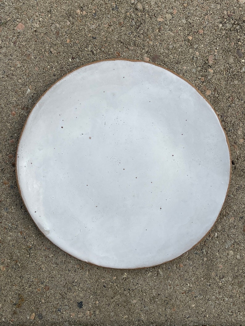 May include: A white ceramic plate with a slightly speckled finish. The plate has a subtle brown rim.