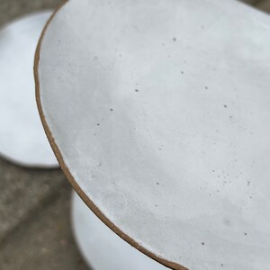 May include: Two white ceramic plates with a brown rim. The top plate is slightly tilted and the bottom plate is visible underneath.