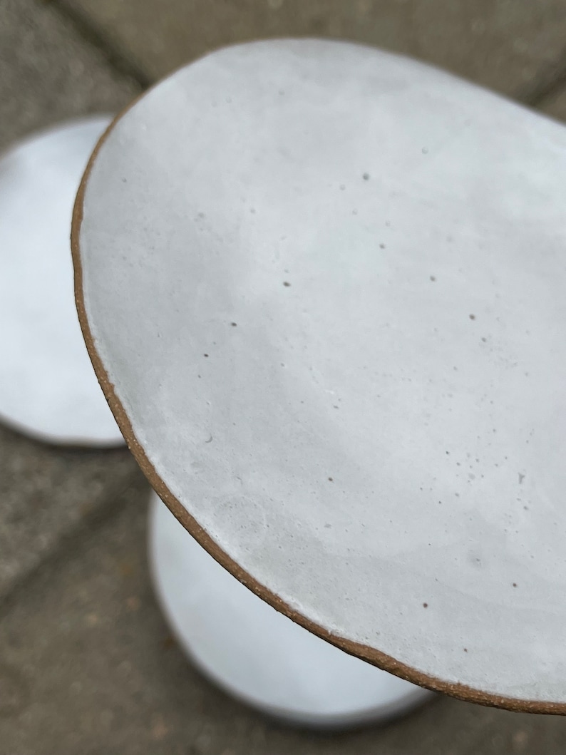 May include: Two white ceramic plates with a brown rim. The top plate is slightly tilted and the bottom plate is visible underneath.