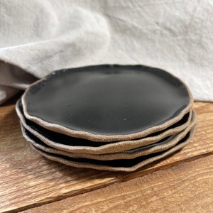 May include: A stack of four black ceramic plates with a brown rim. The plates are stacked on a wooden surface.