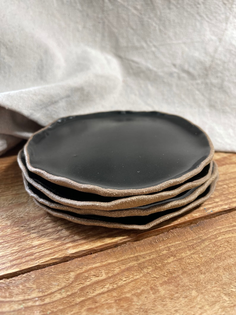 May include: A stack of four black ceramic plates with a brown rim. The plates are stacked on a wooden surface.