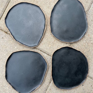 May include: Four black ceramic plates with a slightly irregular, organic shape. The plates have a light brown rim.