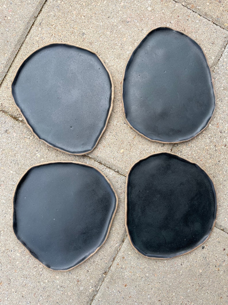 May include: Four black ceramic plates with a slightly irregular, organic shape. The plates have a light brown rim.