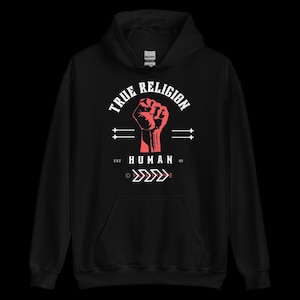 May include: Black hooded sweatshirt with a red fist graphic and the text "TRUE RELIGION" above and "HUMAN 03" below. The design includes arrows and horizontal lines. Made of a soft material.