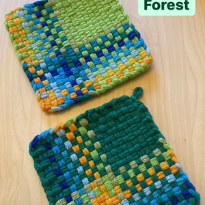 May include: Two woven potholders in shades of green, blue, and orange. The potholders have a square shape and a loop for hanging. The word "Forest" is printed on the top right corner of the image.