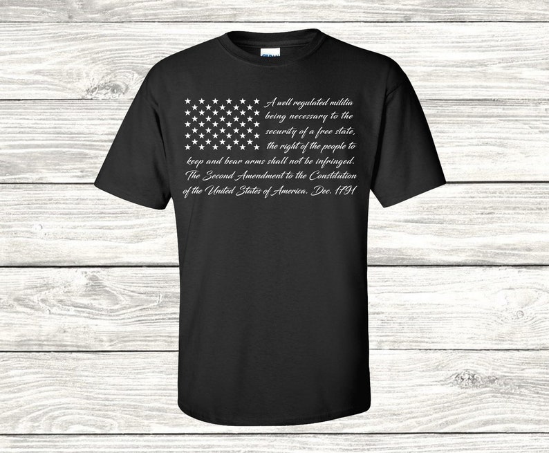 May include: Black t-shirt featuring a white American flag design and the text "A well regulated militia being necessary to the security of a free state, the right of the people to keep and bear arms shall not be infringed. The Second Amendment to the Constitution of the United States of America. Dec. 1791."