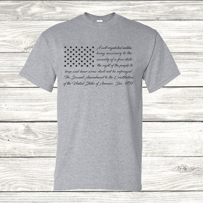May include: A grey t-shirt featuring a black and white image of the American flag and the text "A well regulated militia being necessary to the security of a free state. the right of the people to keep and bear arms shall not be infringed. The Second Amendment to the Constitution of the United States of America. Dec. 1791"