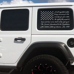 May include: A white Jeep with a black and white American flag decal on the rear window. The decal includes the text of the Second Amendment to the United States Constitution.