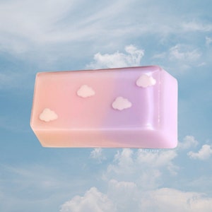 May include: A rectangular, pink and purple soap bar with a gradient effect. The soap has four white cloud shapes embossed on the top.
