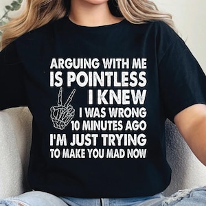 May include: Black t-shirt with white text: "ARGUING WITH ME IS POINTLESS I KNEW I WAS WRONG 10 MINUTES AGO I'M JUST TRYING TO MAKE YOU MAD NOW." The text is above a skeleton hand making a peace sign.