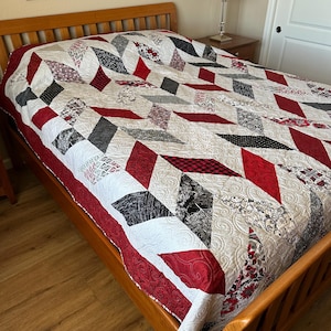 May include: A red, white, and gray chevron patterned quilt on a wooden bed frame. The quilt is made with different fabrics and has a quilted design.