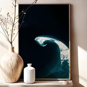 May include: A framed art print featuring an aerial view of a coastal landscape with a dark blue ocean and a white, wave-like formation. A light-colored vase with branches and a small white vase are on a shelf.