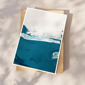 May include: A framed art print featuring a coastal aerial view. The artwork showcases a teal blue ocean meeting a white and light blue landmass. The print is set against a neutral background, with shadows adding depth.