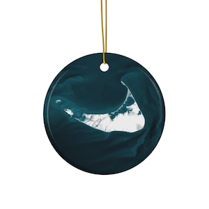 May include: A round, dark teal ceramic ornament with a gold string for hanging. The ornament features a white and teal map of a coastal area, likely a geographical location. The design is a detailed aerial view.