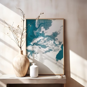 May include: A framed abstract art print with teal and white colors, depicting a geographical landscape. A large wooden vase with branches and a small white vase are on a shelf. The artwork is in a gold frame.