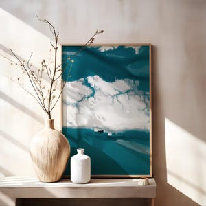 Könnte beinhalten: Gerahmter Kunstdruck mit abstraktem Design in Türkis und Weiß, das an Wolken erinnert. Eine große beige Vase mit Zweigen und eine kleine weiße Vase stehen auf einem Regal. Der Raum wird von natürlichem Licht erhellt.