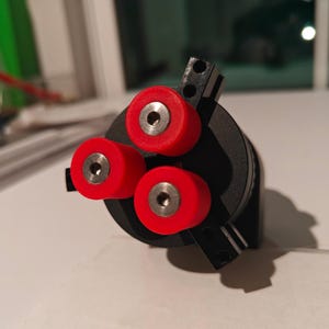 Puede incluir: Un objeto impreso en 3D negro y rojo con tres ruedas rojas. Las ruedas tienen un pequeño centro metálico.