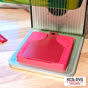 May include: A red plastic mould for creating livestock ID tags. The mould is on a silver platform with a ruler and the text "LIVESTOCK ID" and "GOOD FOR 150 TAGS".