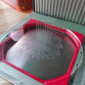 May include: A red and clear plastic frame with a clear glass plate inside. The glass plate has the words "Merry Christmas" etched into it.