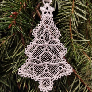 May include: White lace Christmas tree ornament with a star at the top. The ornament is hanging from a white ribbon on a green pine tree branch.