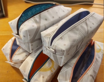 May include: Five white zippered pouches with different coloured linings. The pouches have a white background with a grey and white pattern. The pouches are stacked on top of each other.