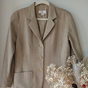 May include: A tan and brown houndstooth blazer with a notched collar, three buttons, and two front pockets. The blazer is hanging on a white hanger. The label reads "JOSEPH ABBOUD".