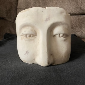 Peut inclure: Planteur en plâtre blanc en forme de visage avec deux yeux et un nez.