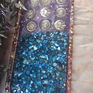 May include: A purple resin tray with a glittery gold border. The tray is filled with blue iridescent mosaic tiles and silver sun and moon charms.