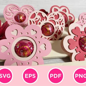 May include: Pink and red paper flower-shaped holders with heart cutouts, each holding a wrapped chocolate. The holders are arranged on a light-colored surface, with a paper flower in the background. The image includes the text "SVG", "EPS", "PDF", and "PNG".