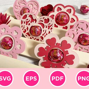 May include: Pink and red paper cutouts in heart and flower shapes, each holding a wrapped chocolate. The cutouts are arranged on a light-colored surface, with a paper flower and the words "SVG", "EPS", "PDF", and "PNG" in pink circles.
