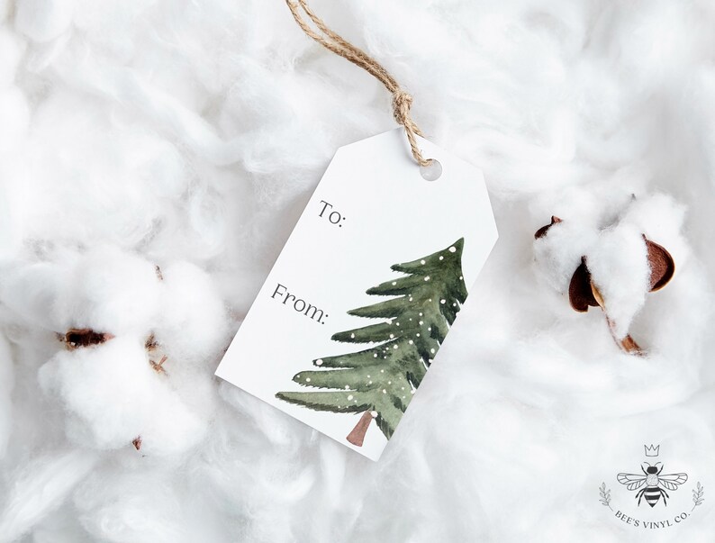 May include: White gift tag with a watercolor illustration of a green pine tree with snow on it. The tag has the words "To:" and "From:" printed on it.