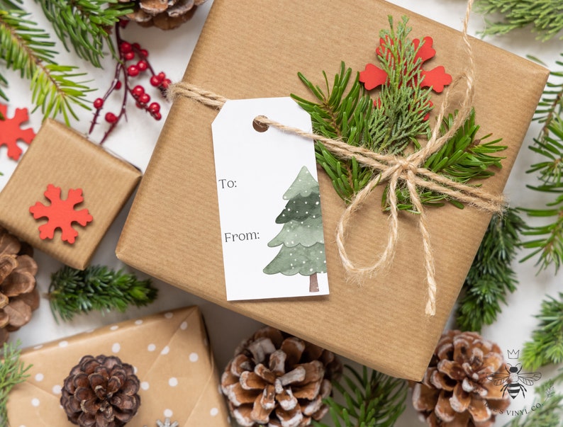 May include: A brown gift box wrapped with twine and decorated with a green pine sprig, a red snowflake, and a watercolor illustration of a Christmas tree. The gift tag says "To:" and "From:".