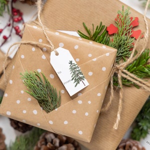 May include: Two brown paper gift boxes wrapped with twine and decorated with white polka dots, green sprigs, and red paper snowflakes. One box has a gift tag with a small tree illustration and the words "To:" and "From:".
