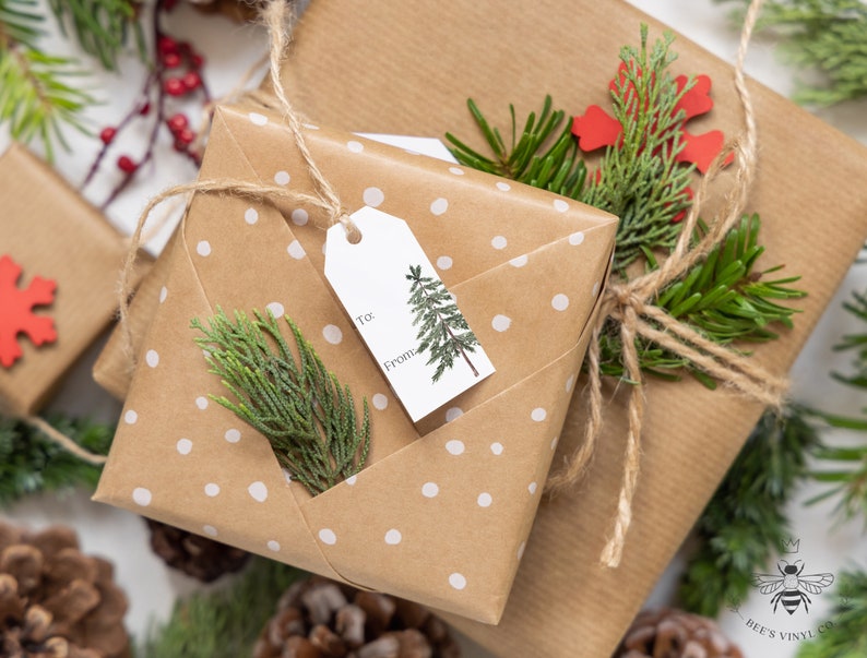 May include: Two brown paper gift boxes wrapped with twine and decorated with white polka dots, green sprigs, and red paper snowflakes. One box has a gift tag with a small tree illustration and the words "To:" and "From:".