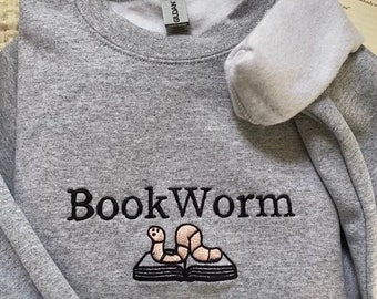 May include: Gray sweatshirt with a black embroidered design of a bookworm reading a book. The text "Book Worm" is embroidered above the bookworm.