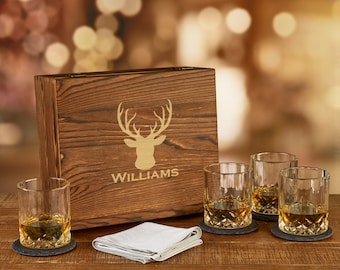 May include: A wooden box with a deer silhouette and the name "WILLIAMS" engraved on the front. The box contains four clear glass whiskey tumblers with a diamond pattern and four black coasters.
